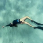 nurkująca kobieta relaksuje się na dnie morza podczas sesji freedivingu, który może być formą medytacji, a nawet terapii.